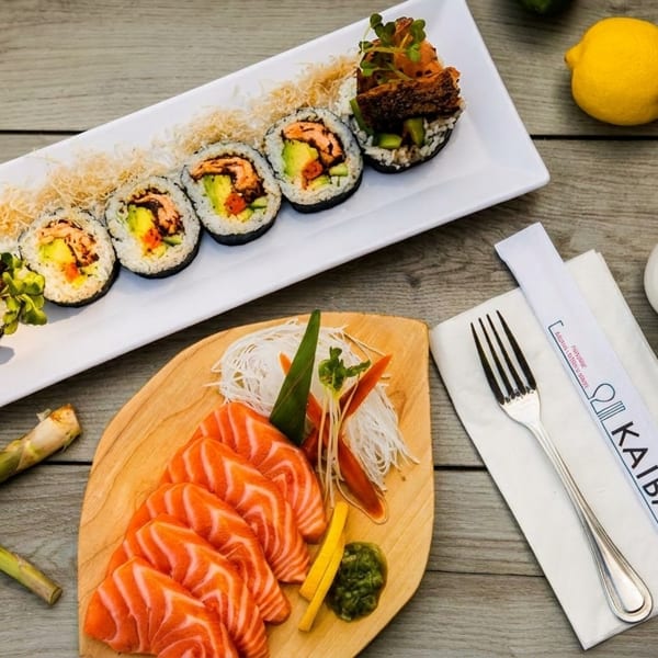 A Kaiba restaurant meal with sushi rolls, salmon sashimi, and asparagus on a wooden table.
